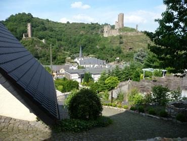 A picturesque landscape with a view of a medieval castle and a small village. Surrounded by green hills and bright blue sky.