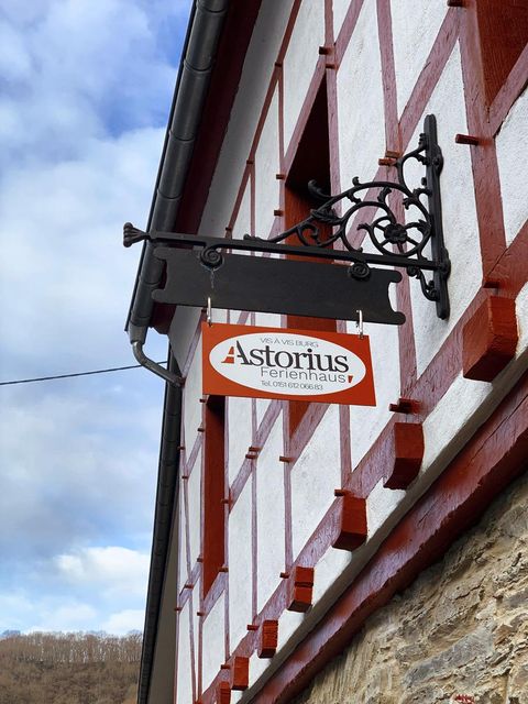 Ein rustikales Gebäude mit rotem Fachwerk und einem Schild, das "Astorius Ferienhaus" anzeigt. Der Himmel ist bewölkt und es wirkt einladend.