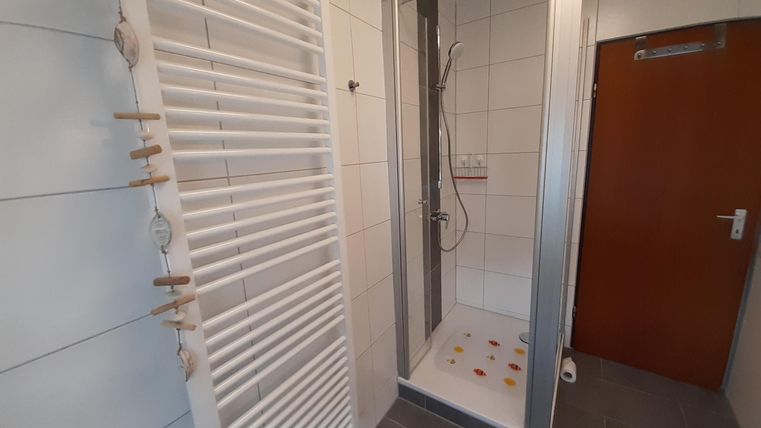 Ein modernes Badezimmer mit einer Dusche und einem Handtuchwärmer. Der Fußboden ist grau und die Wände sind hell gefliest.