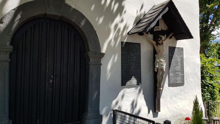 A historic building with a dark wooden door and a statue on the wall. Next to the statue are two memorial plaques.