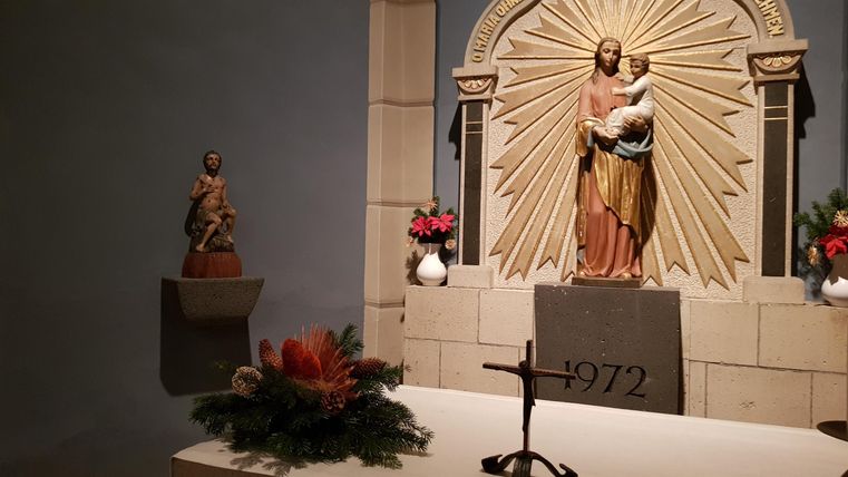 An altar with a statue of Jesus and a child, surrounded by flowers. In the background, decorative elements and a small statue are visible.