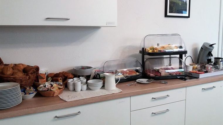 A buffet with various breakfast items, including rolls, jam, and cheese. There is also a coffee machine and several cups on the table.