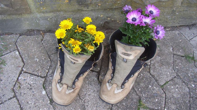 Ein Paar alte Stiefel mit bunten Blumen. Die Stiefel stehen auf einem Pflastersteinboden.