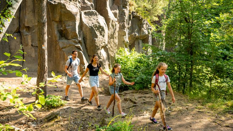 Family hiking on a forest path with rocks in the background.