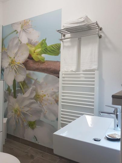 A modern bathroom with a wall decoration of flowers and a stylish sink. Towels and a towel holder provide a practical and appealing setup.