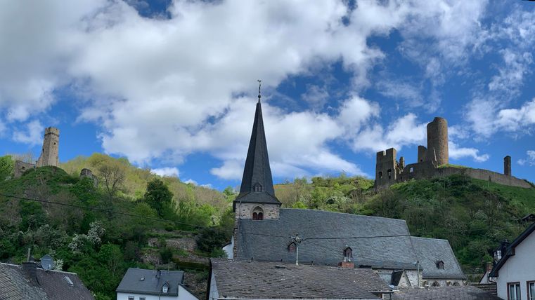 Eine malerische Aussicht auf eine Landschaft mit alten Burgen und einem Kirchturm. Der Himmel ist blau mit einigen weißen Wolken.