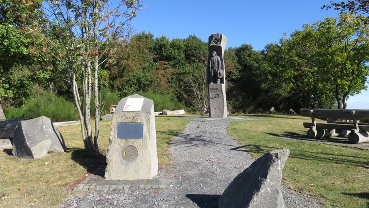Ein Denkmal mit einer Statue und Gedenktafeln in einem Park mit Bäumen und einem Picknicktisch.