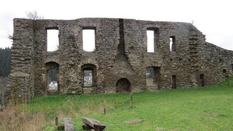 An old stone ruin, surrounded by green grass. The building has several window openings and shows signs of time.