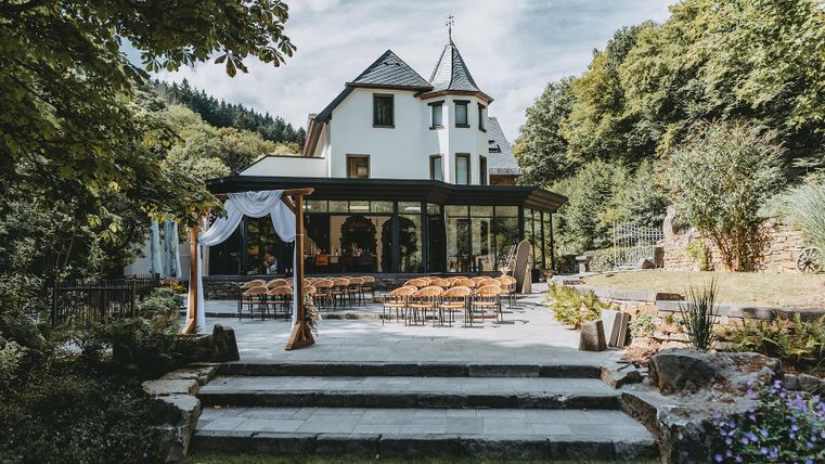 Ein elegantes Gebäude mit einem Glasbalkon und einer schönen Terrasse. Der Garten ist gepflegt und lädt zu Veranstaltungen im Freien ein.