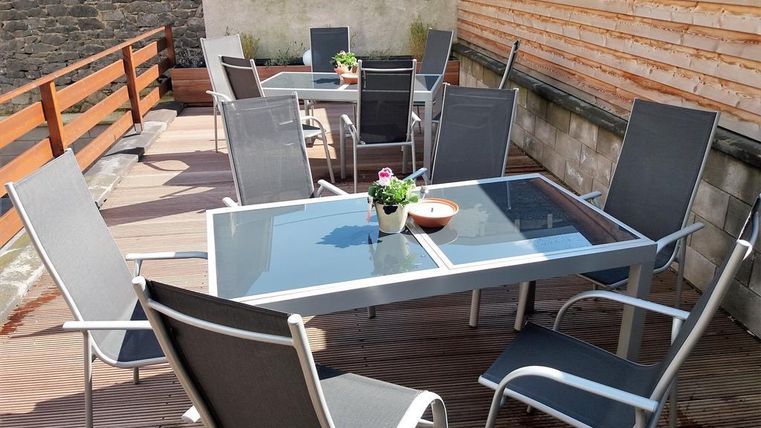 A cozy outdoor area with several tables and chairs. The tables are decorated with flowers and surrounded by wooden planks.