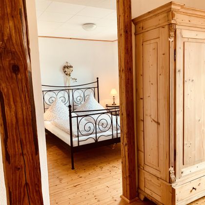 Ein gemütliches Schlafzimmer mit einem metallenen Bett und einem großen Holzschrank. Der Raum hat warme Holztöne und eine einladende Atmosphäre.