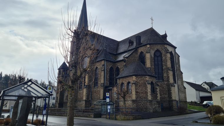 Eine alte Kirche mit einem hohen Turm. Sie steht an einer Straßenkreuzung in einer ländlichen Gegend.