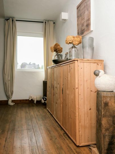 A bright hallway with a wooden cabinet and decorative flowers. The walls are painted in neutral colors and there is a window that lets in daylight.