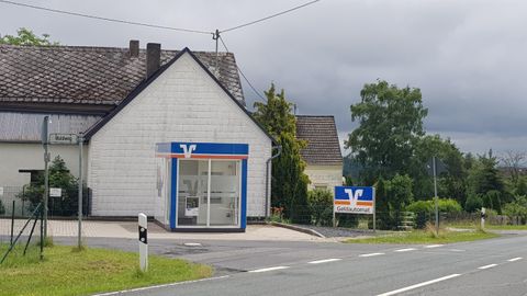 Ein kleines Geschäft an einer Landstraße mit einem klaren blauen Himmel. Neben dem Gebäude steht ein großes Hinweis- schild.