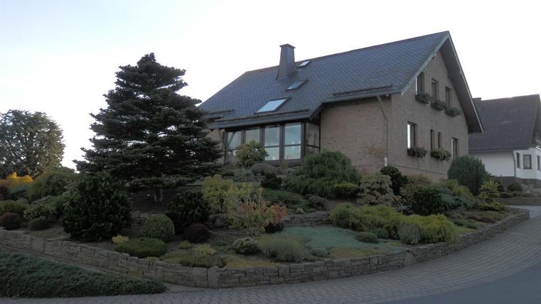 A modern house surrounded by well-maintained bushes and trees. The entrance area is elegantly designed with an appealing landscaping.