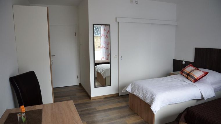 A simple bedroom with a single bed and a small table. The room has a modern look and wooden flooring.