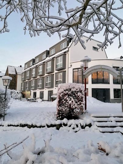 Ein modernes Gebäude im Schnee, umgeben von einem schneebedeckten Garten. Der Himmel ist klar und die Atmosphäre ist winterlich.