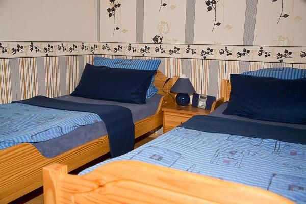 Ein gemütliches Schlafzimmer mit zwei Einzelbetten und blauen Bettdecken. Die Wände sind mit einem dezenten Blumenmuster dekoriert.