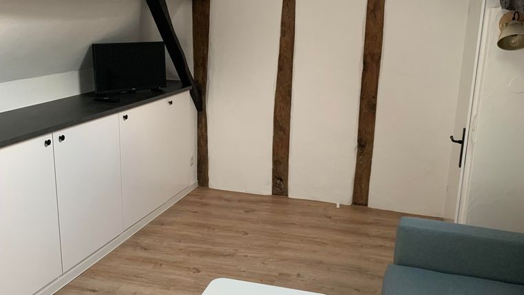 Ein gemütlicher Raum mit einem hellen Holzboden und schrägen Wänden. Ein graues Sofa und ein kleiner Tisch ergänzen die Einrichtung.