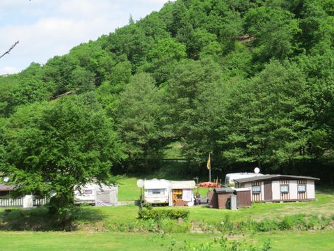 Ein ruhiger Campingplatz in der Natur, umgeben von grünen Hügeln. Mehrere Wohnwagen stehen in einer idyllischen Umgebung.