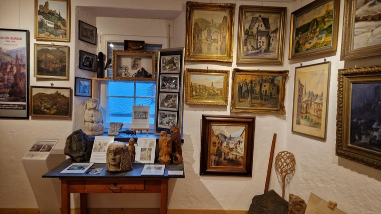 Ein gemütlicher Raum mit vielen Bilderrahmen an den Wänden. In der Mitte steht ein Tisch mit verschiedenen Kunstwerken und Informationsmaterialien.