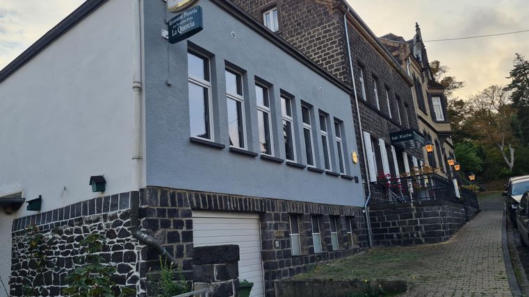 Ein charmantes Gebäude mit einem grauen Fassadenanstrich in einer ruhigen Straße. Die Umgebung ist grün und einladend.