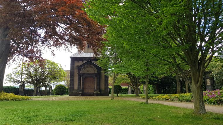 Ein ruhiger Park mit grünen Bäumen und bunten Blumen. Im Hintergrund steht ein historisches Gebäude.