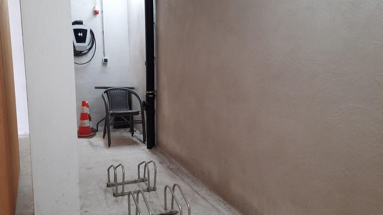A narrow corridor with a chair and two bike racks. The walls are smooth and the lighting is bright.