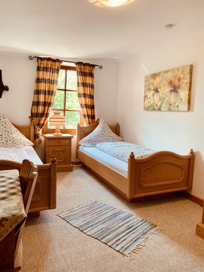 Ein gemütliches Schlafzimmer mit zwei Einzelbetten und einer Holzkommode. Die Fenster sind mit karierter Gardine dekoriert und ein Teppich liegt auf dem Boden.
