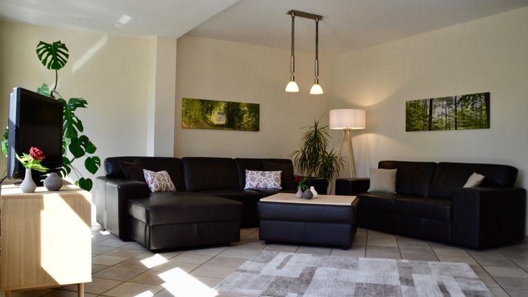 Ein modernes Wohnzimmer mit einer dunklen Couch und einem Couchtisch. An der Wand hängen Bilder und eine Pflanze sorgt für eine gemütliche Atmosphäre.