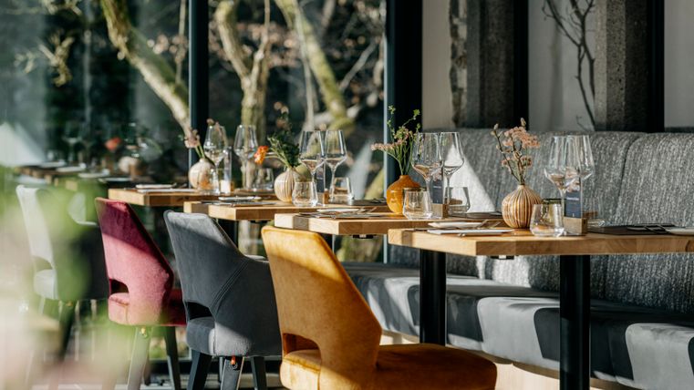 A modern restaurant with elegantly set tables and colorful chairs. Large windows let in plenty of daylight and create an inviting atmosphere.