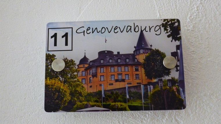 A sign with the inscription "Genovevaburg" and the number 11. In the background, a castle with gardens can be seen.
