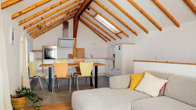 Eine moderne Küche mit Holzbalkendecke und gemütlichem Wohnbereich. Der Raum ist hell und einladend, mit einem großen Sofa und einem Esstisch.