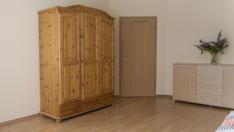A simple room with a wooden closet and a dresser. A vase with flowers stands on the wall.