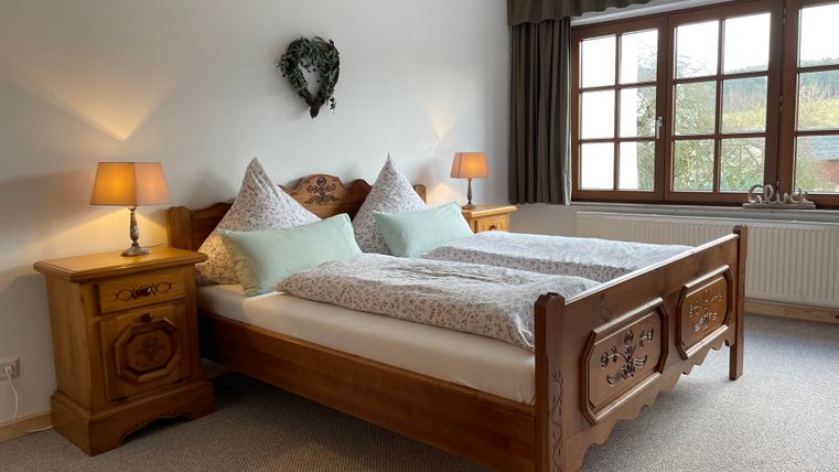 Ein gemütliches Schlafzimmer mit einem großen Holzbett und zwei Nachttischen. Das Zimmer hat sanftes Licht von den Tischlampen und große Fenster mit Blick nach draußen.