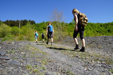 Vier Wanderer in einer ehemaligen Schiefergrube mit grünen Bäumen und blauem Himmel