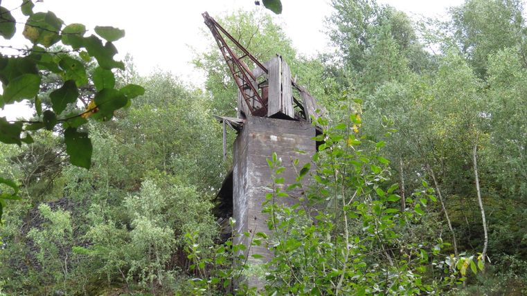 Eine verlassene Mühle, umgeben von üppigem Grün und Bäumen. Die Struktur ist teilweise verwittert und von der Natur zurückerobert.