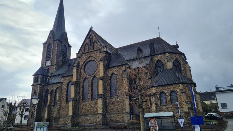 Eine beeindruckende Kirche mit einem hohen Turm und gotischen Elementen. Der Himmel ist bewölkt und die Umgebung wirkt ruhig.