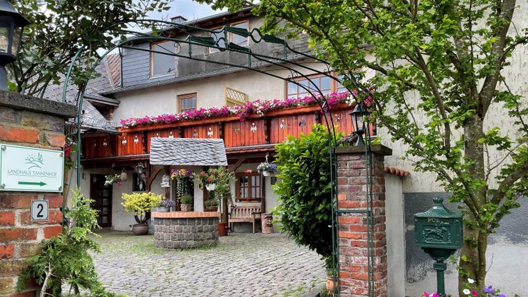 Ein einladender Innenhof mit einem gepflasterten Weg und bunten Blumen. Im Hintergrund sieht man ein charmantes Gebäude mit Holzdetails und einen gemütlichen Sitzecke.