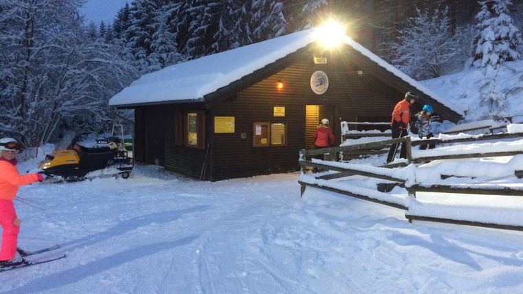 Eine gemütliche Hütte im Schnee, umgeben von Tannenbäumen. Skifahrer genießen die winterliche Landschaft.