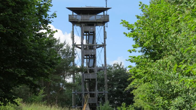 A wooden observation tower in the countryside, surrounded by trees and meadows.