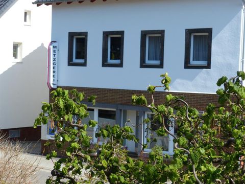 Ein Metzgerei-Geschäft in einem Wohngebiet. Die Fassade ist weiß mit großen Fenstern und einem Schilder mit dem Wort "Metzgerei".