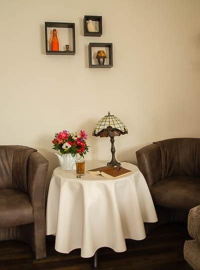 Ein gemütlicher Sitzbereich mit zwei beigen Sessel und einem runden Tisch. Auf dem Tisch steht eine Tischlampe, Blumen und ein Glas Getränk.