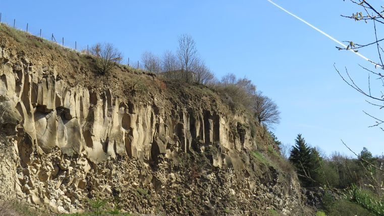 Eine steile Klippe mit ausgewaschenen Felsen und Bäumen. Der Himmel ist klar und blau, und es gibt einige Wolkenstreifen.