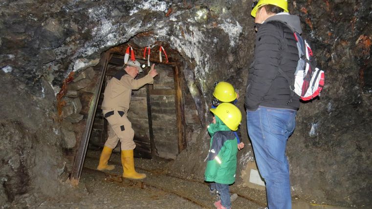 Eine unterirdische Mine mit einem Führer und zwei Besuchern. Alle tragen Sicherheitshelme und schauen zur Mine hinein.