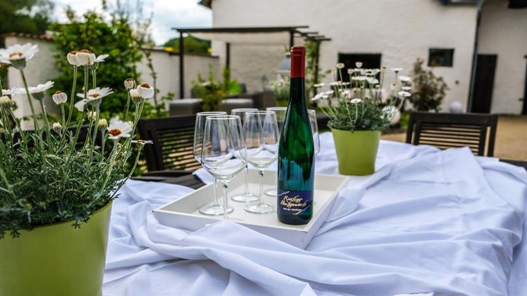 A beautifully set table outside with a bottle of wine and glasses. Surrounded by fresh flowers in green pots.