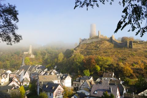 A picturesque landscape with a small town and an old castle ruin in the fog. The colors of the trees display autumn.
