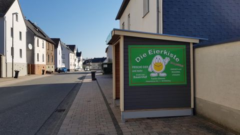 Ein Stadtbild mit Häusern und einem Schild, das für die „Eierhütte“ wirbt. Es ist sonnig und der Himmel ist klar.