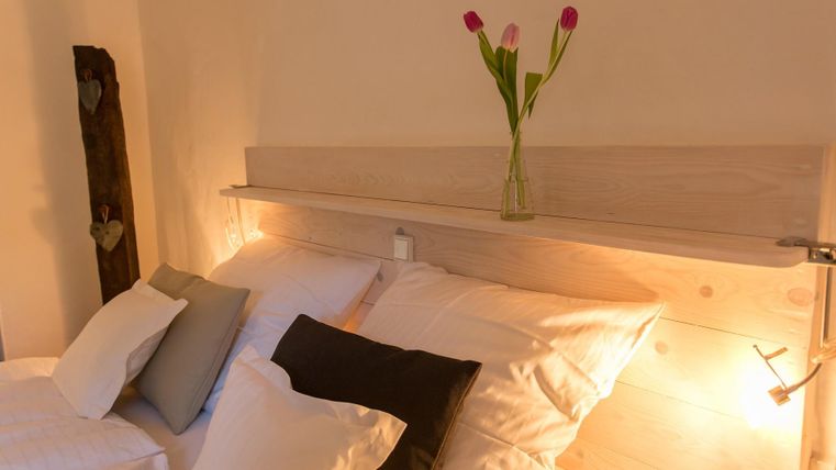 A cozy bedroom with two beds and many pillows. On the nightstand, there is a vase with fresh tulips.