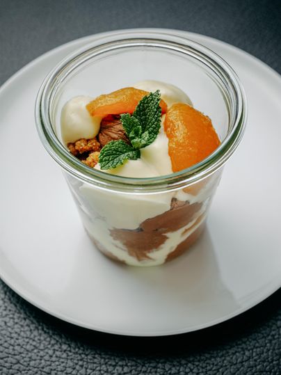 Ein köstliches Dessert in einem Glas mit Joghurt, Mandarinen und Knusperstücken. Mit einem Zweig frischer Minze garniert.